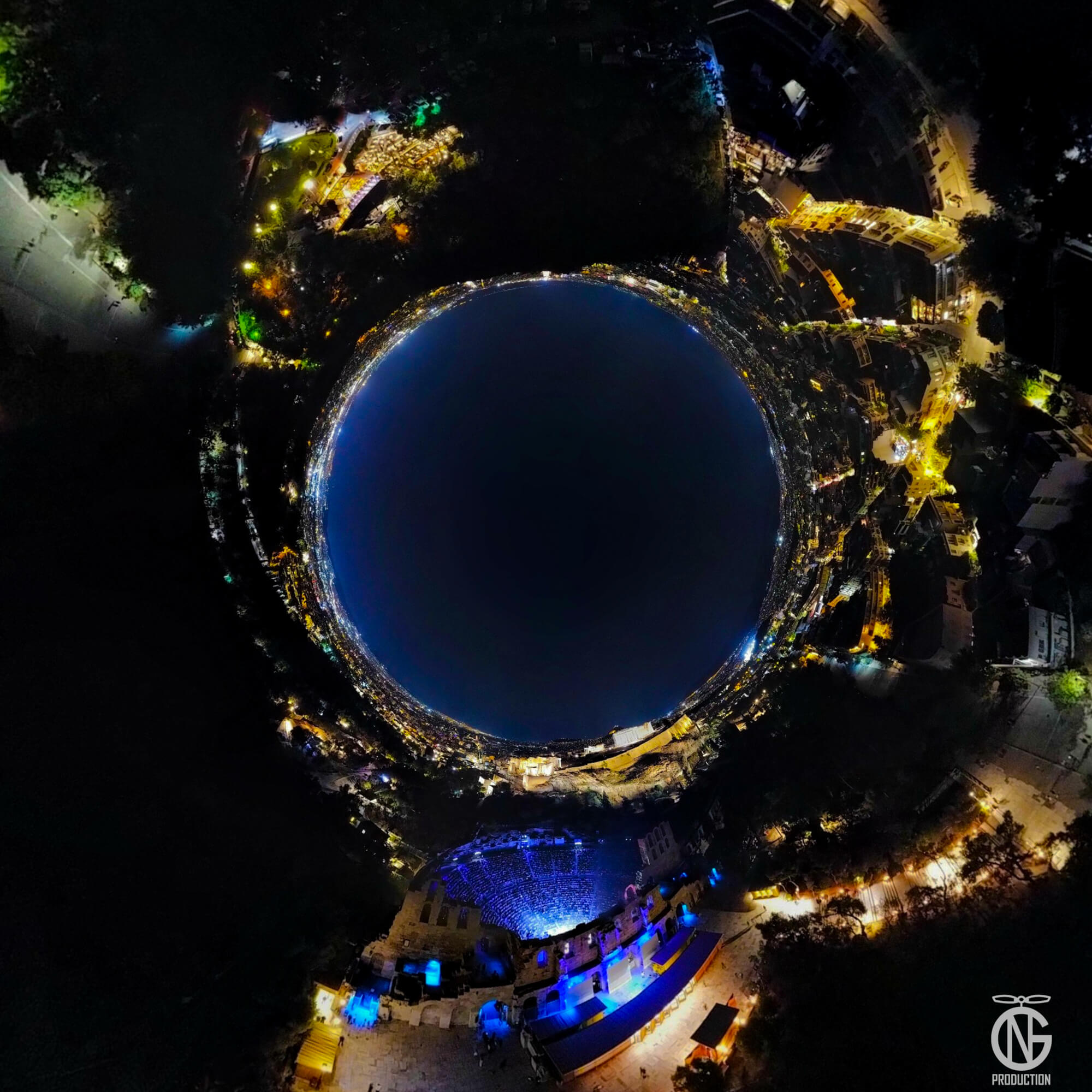 Night tiny-planet 360° view of the Herodes Atticus Odeon (Herodion)—amber-lit marble tiers around a deep-blue sky on the Acropolis slope.