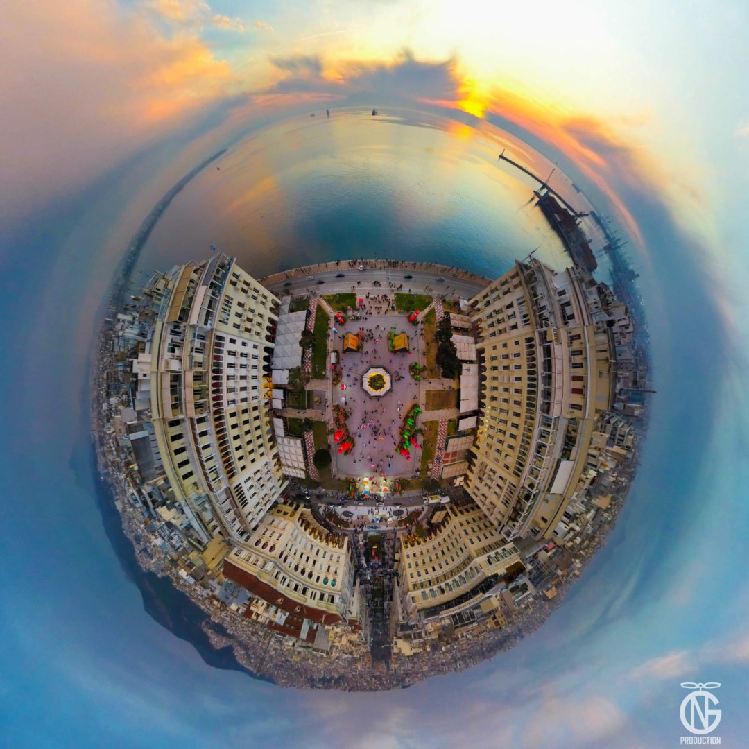 Golden-hour tiny-planet 360° drone view of Aristotelous Square with the Christmas tree, festive stalls and the Thermaic Gulf at sunset.