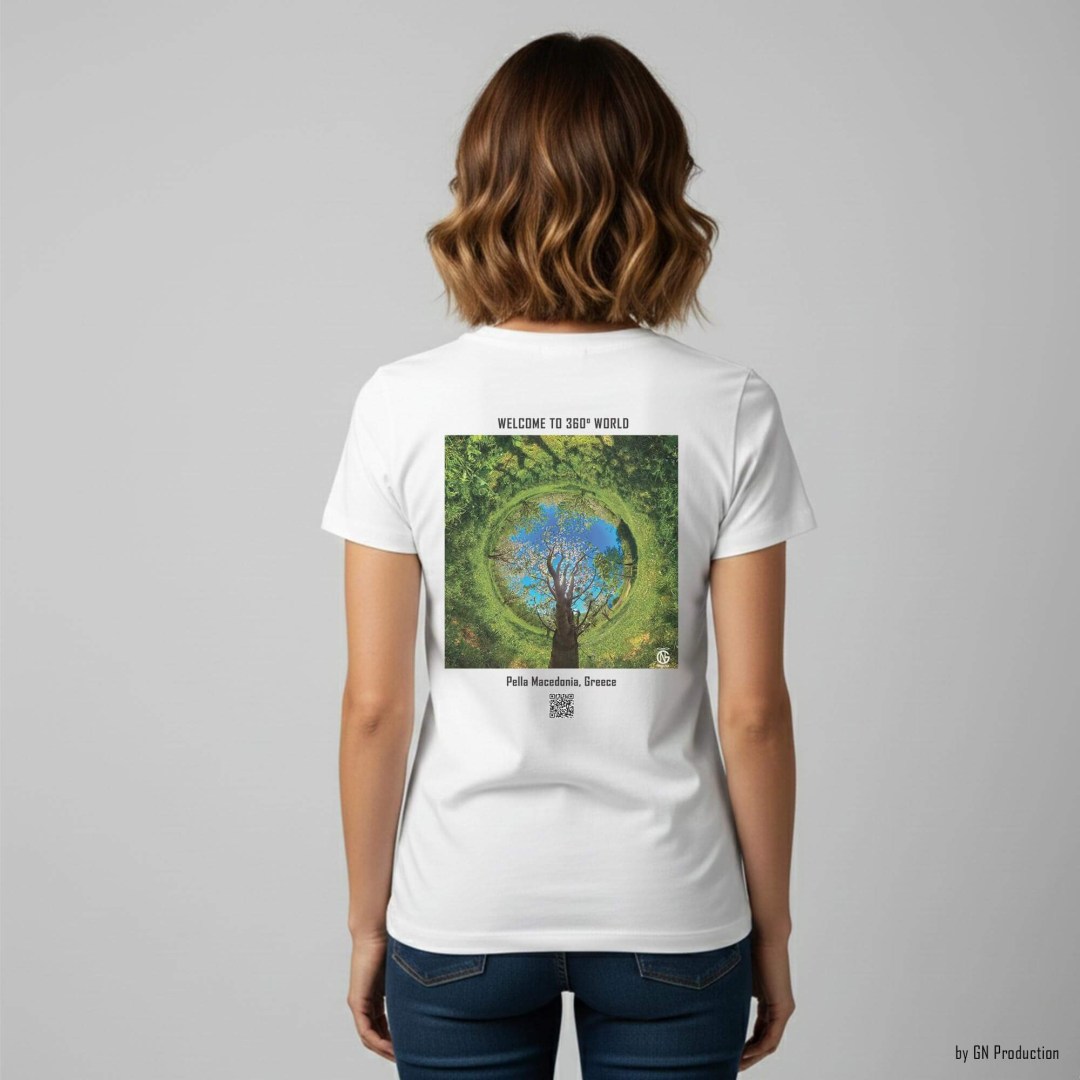 Woman model wearing white art T-shirt featuring Pella cherry orchard inverted tiny-planet 360° artwork, spring blossoms forming a green circular landscape, wearable art by GN Production.
